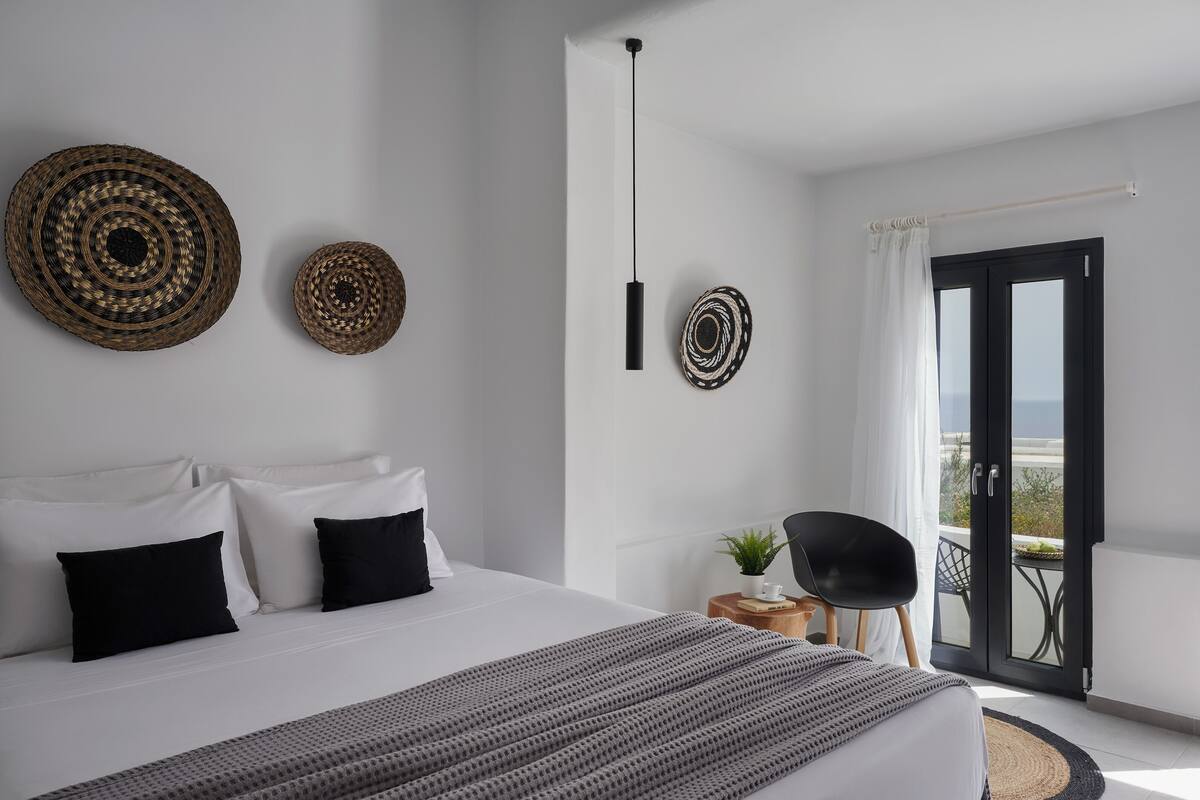 Habitación de hotel moderna con una cama grande, dos cestas tejidas colgadas en la pared, una mesita de noche con una planta y un balcón con una silla.