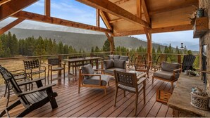 Eine Holzterrasse mit Gartenmöbeln, einem Kamin aus Stein und Blick auf einen bewaldeten Bergrücken.