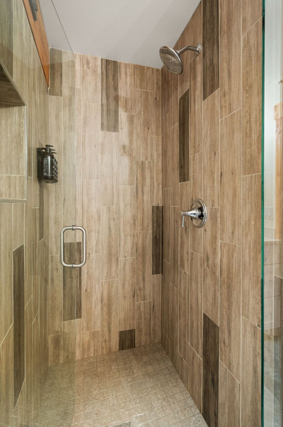 Un espace douche équipé d’un pommeau de douche à main, d’un distributeur de savon à main et d’une porte en verre.