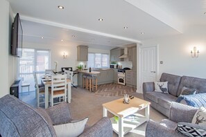 A modern living room with a grey sofa, a coffee table, and a dining area with a table and chairs. - Betteridge View Lodge - a holiday lodge that sleeps 6 guests in 3 bedrooms (Windermere)