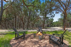 A campfire with two Adirondack chairs in a forested area.