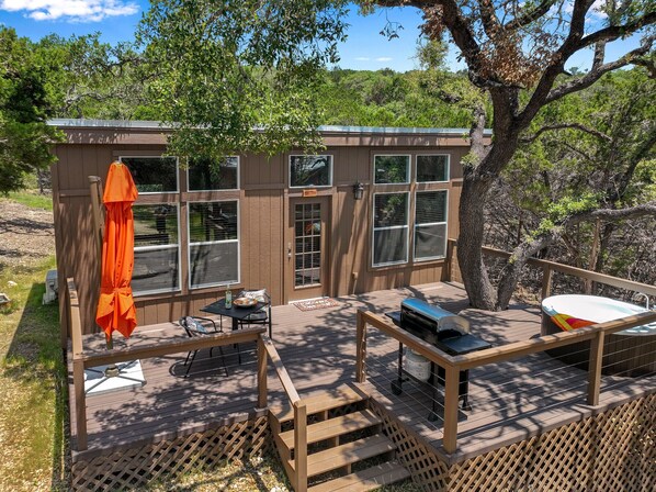 Una cabaña pequeña con terraza, una parrilla y una zona de estar al aire libre.