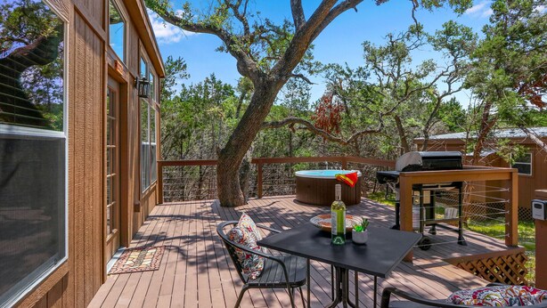 Une terrasse en bois avec une table et des chaises, un barbecue et un jacuzzi.
