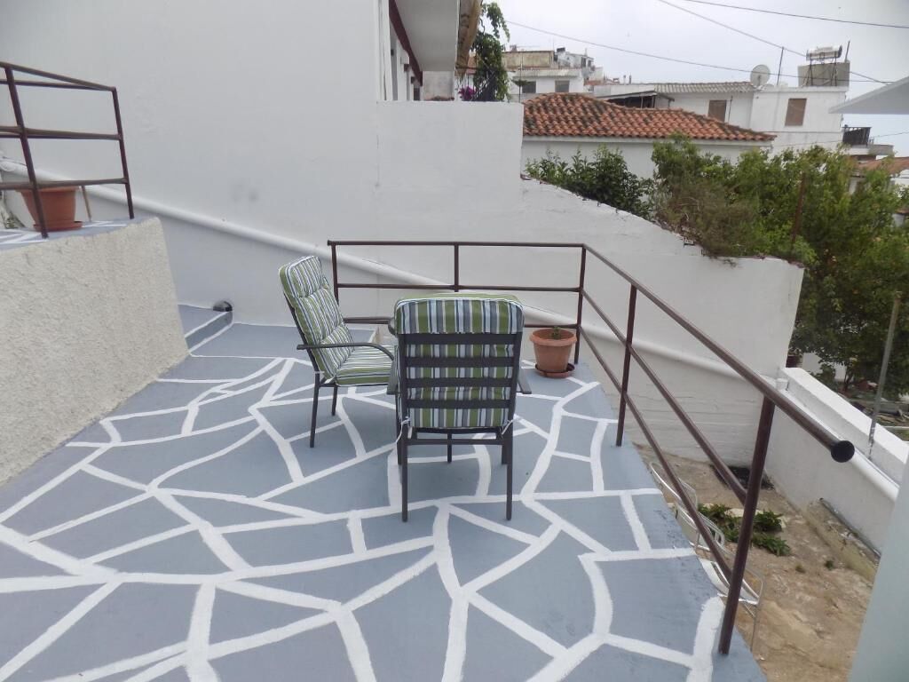 Ein Balkon mit einem geometrisch gemusterten Boden, einem gestreiften Stuhl und einem kleinen Tisch.