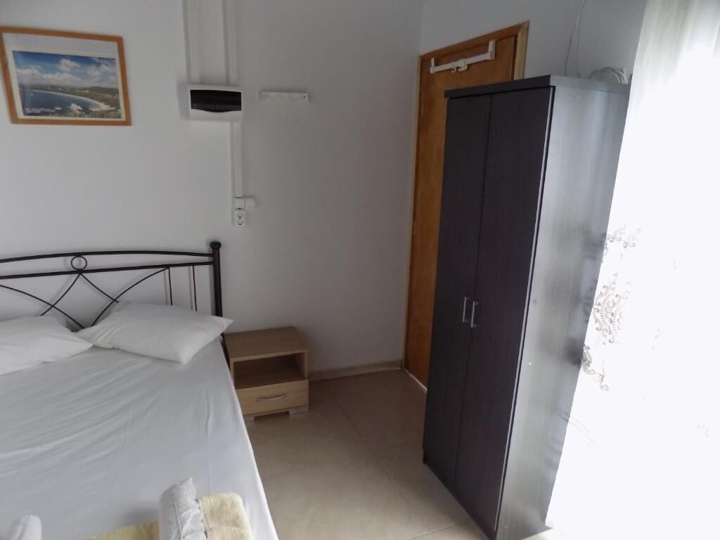 A bedroom with a bed, a wardrobe, a small wooden cabinet, and a framed picture on the wall.