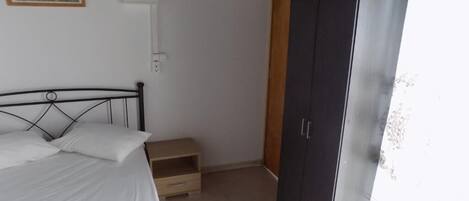 A bedroom with a bed, a wardrobe, a small wooden cabinet, and a framed picture on the wall.