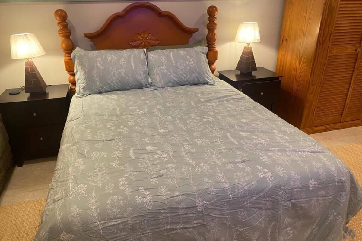 A bed with a floral bedspread, two bedside tables with lamps, and a wooden wardrobe.