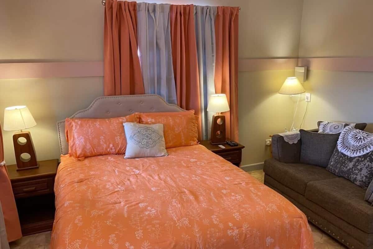A bedroom with a bed, two bedside tables with lamps, a nightstand, a sofa, and a window with curtains.