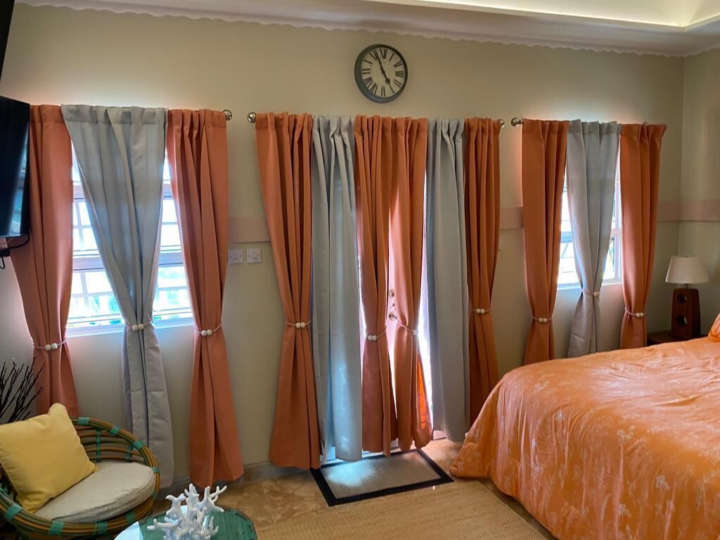 A bedroom with a bed, curtains, a clock, and a chair.