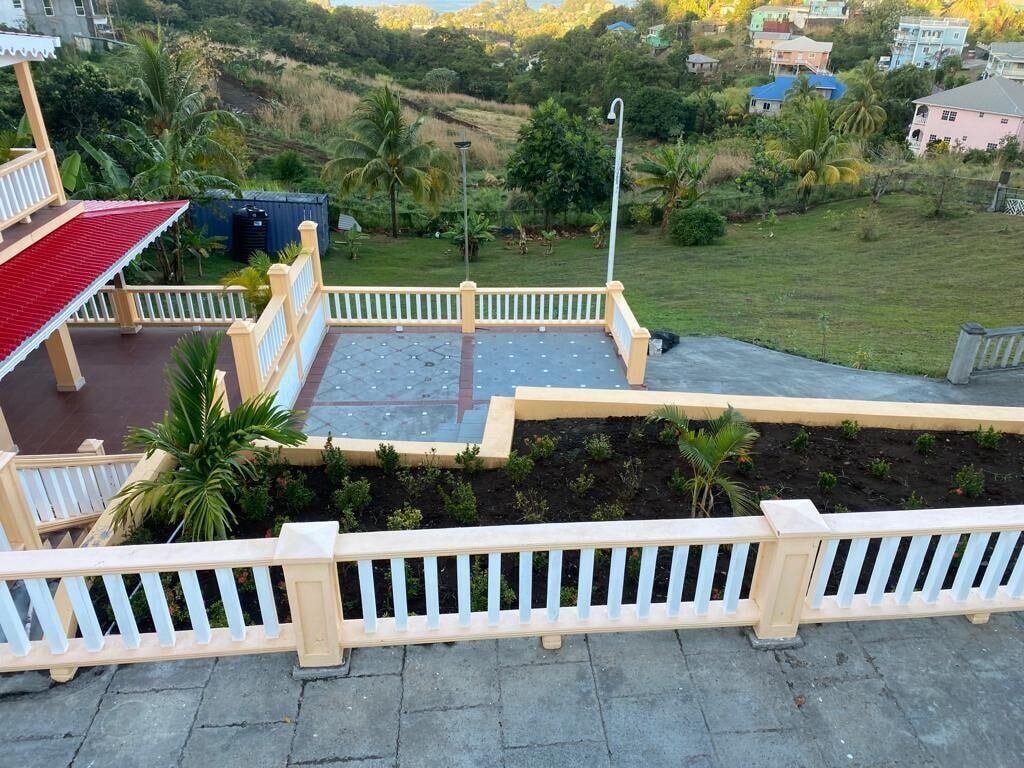 A terrace with a view of a green landscape, a white railing, and a red roof.