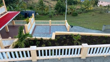 A terrace with a view of a green landscape, a white railing, and a red roof.