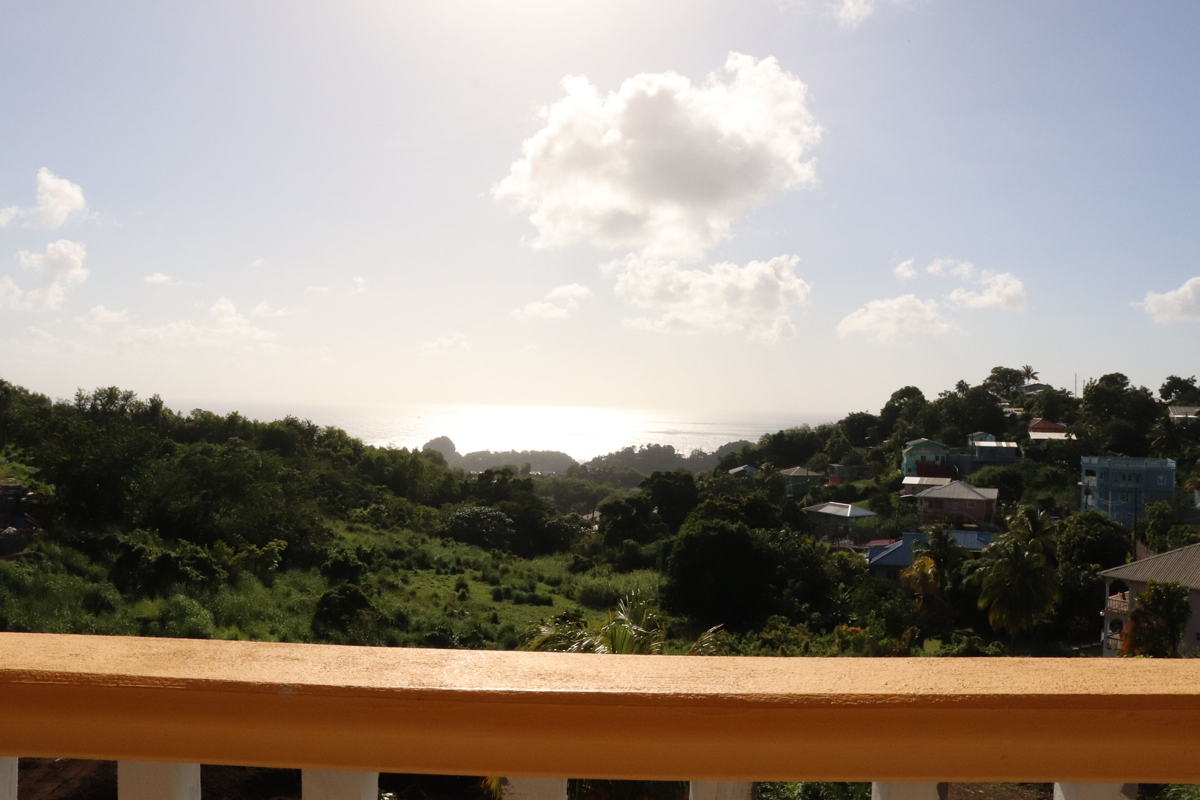 Un balcon donnant sur un paysage verdoyant et sur des maisons situées au loin.
