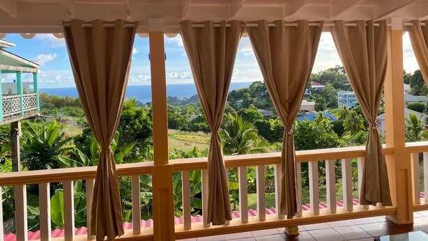 A balcony with curtains, a view of a lush landscape, and a building in the background. - Dalys Luxury Apartments (Choppins)