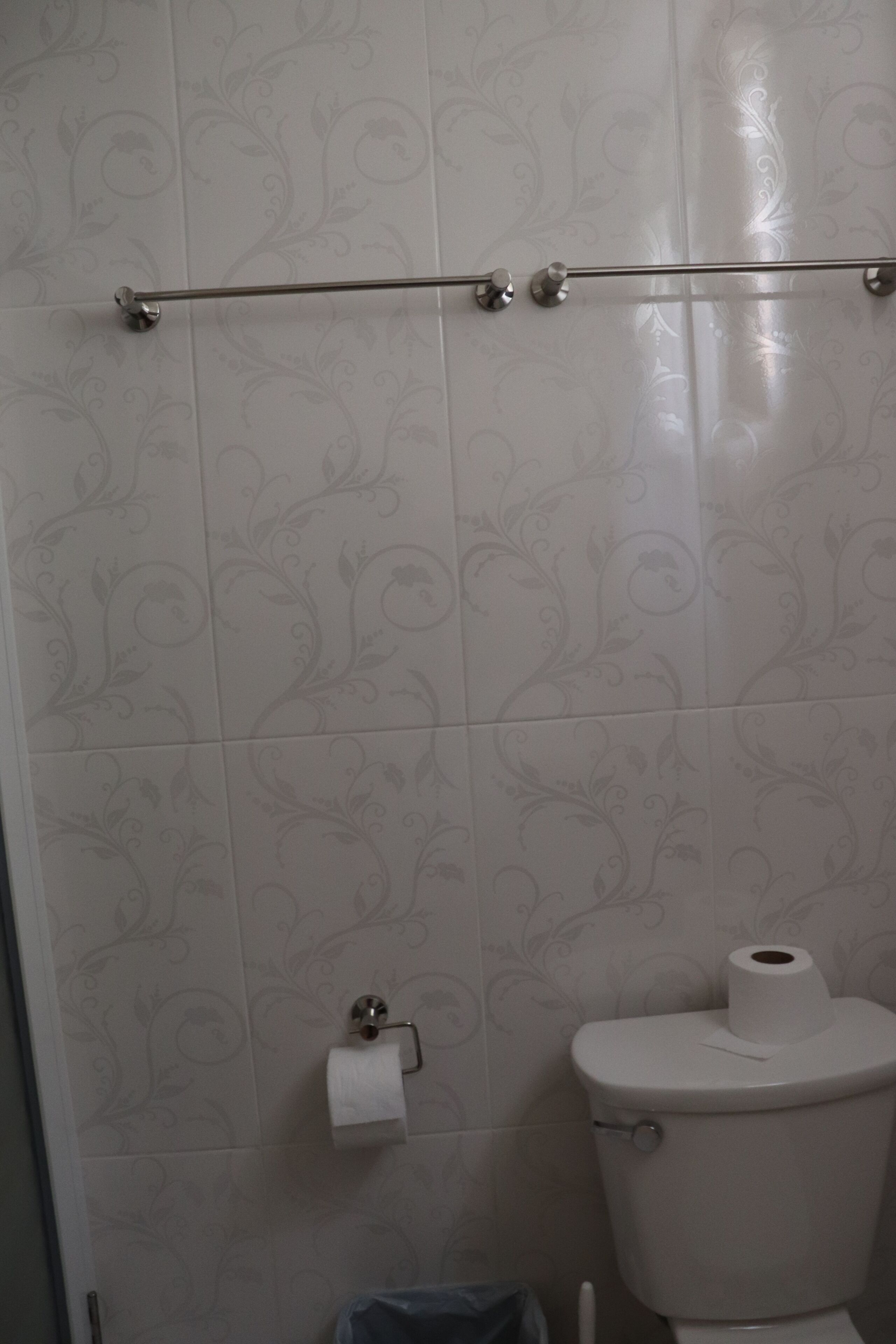 A bathroom with a toilet, a towel rack, and a toilet paper holder on the wall.