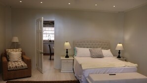 A bedroom with a bed, two bedside tables with lamps, a chair, and a door leading to another room. - Dalys Luxury Apartments (Choppins)