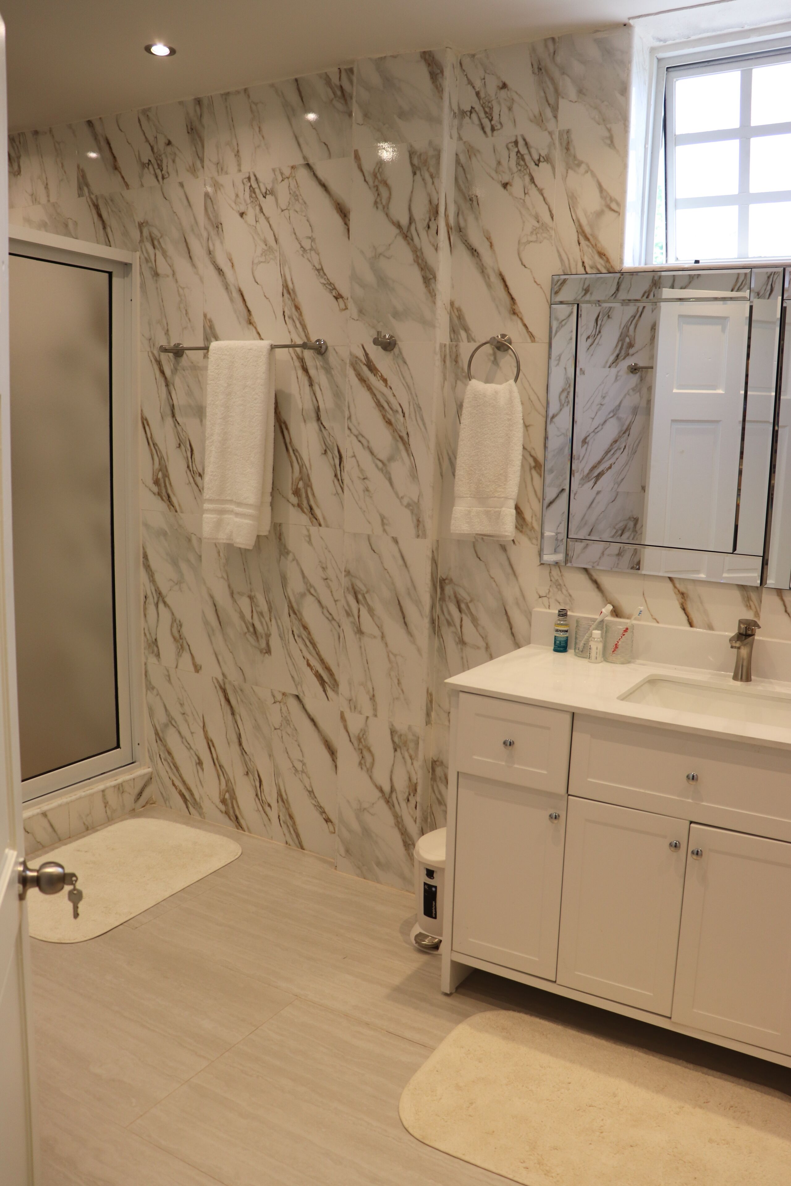 Une salle de bain avec des murs en marbre, un meuble-lavabo blanc, un évier et un porte-serviettes.