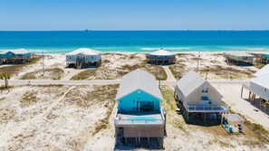 A beachfront property with multiple houses on stilts, a swimming pool, and a clear view of the ocean.