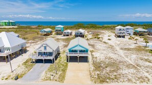 A beachfront property with multiple houses elevated on stilts, a sandy beach, and the ocean in the background. - Gulf Views | Private Pool | Pet Friendly | Beach Access (Gulf Shores)