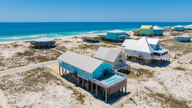 A coastal property with multiple beachfront houses, some elevated on stilts, featuring outdoor seating areas and a swimming pool. - Gulf Views | Private Pool | Pet Friendly | Beach Access (Gulf Shores)