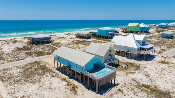 A coastal property with multiple beachfront houses, some elevated on stilts, featuring outdoor seating areas and a swimming pool.