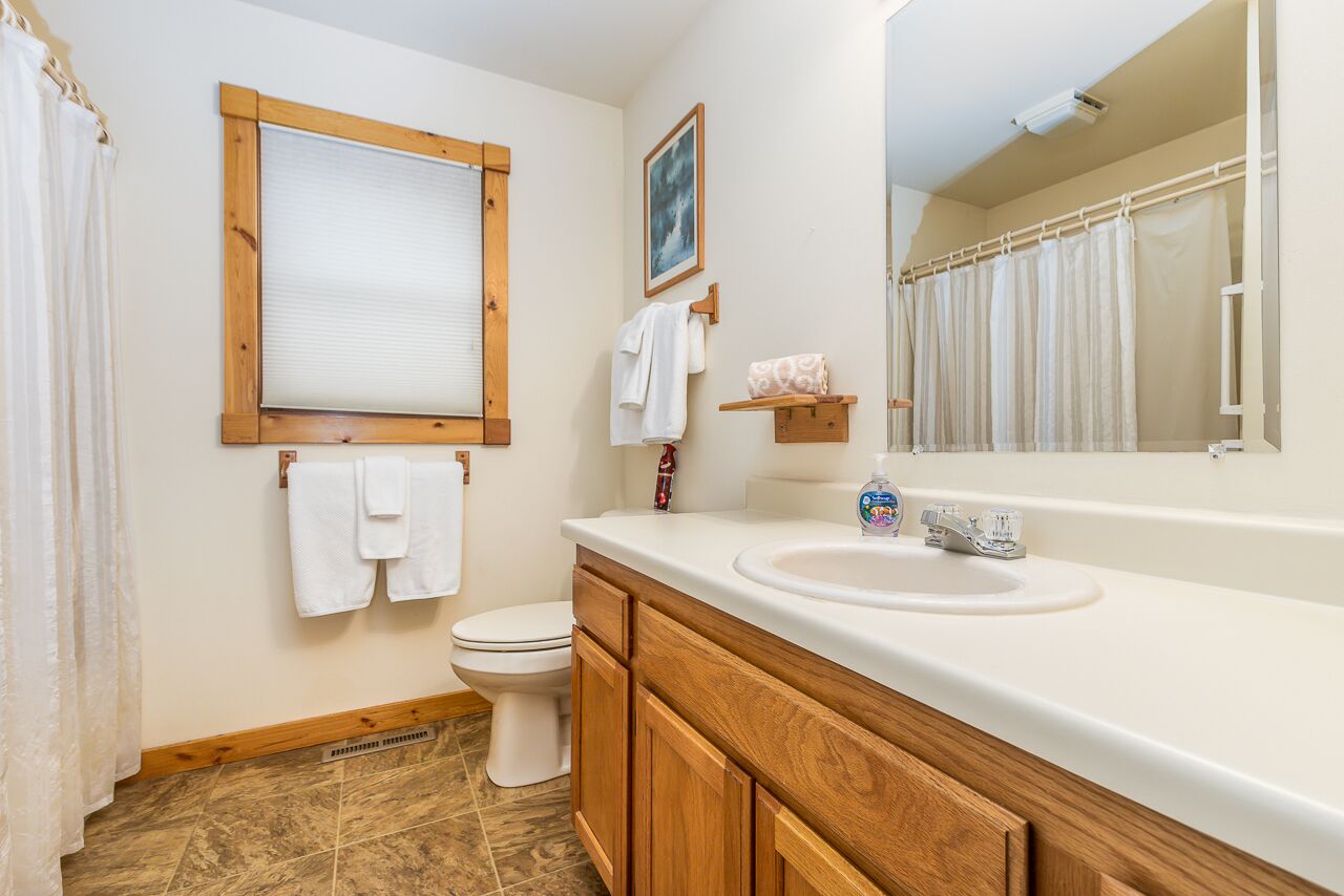 A bathroom with a wooden vanity, a sink, a toilet, and a window with a wooden frame.
