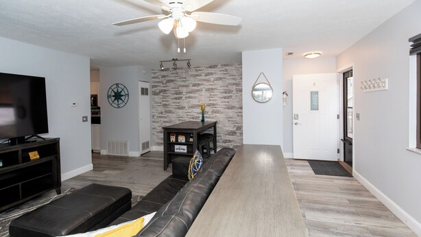 A modern living room with a long wooden table, a black leather sofa, a television, and a ceiling fan. - Dual Townhomes in Central Downtown Huron (Huron)