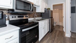 A modern kitchen with white cabinets, a stainless steel refrigerator, a microwave, and a stove. - Dual Townhomes in Central Downtown Huron (Huron)