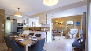 A modern kitchen with a dining area, wooden walls, and a cozy living space with a sofa and chairs. - 200m from ski slopes, floor -2, terrace, fireplace or stove, parking, tv, ski locker, 80m² (Les Deux Alpes)