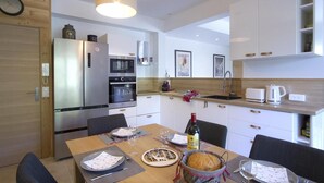 A modern kitchen with a wooden wall, stainless steel appliances, a dining table set for two, and a hanging light fixture. - 200m from ski slopes, floor -2, terrace, fireplace or stove, parking, tv, ski locker, 80m² (Les Deux Alpes)