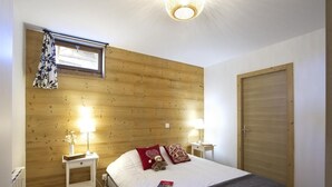 A bedroom with a wooden headboard, two bedside tables with lamps, a bed with a red pillow, and a closed door. - 200m from ski slopes, floor -2, terrace, fireplace or stove, parking, tv, ski locker, 80m² (Les Deux Alpes)