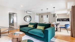 A modern living room with a green sofa, a beige armchair, and a wooden coffee table. There is a kitchen area in the background with a dining table and chairs. - Nestled along the Que banks of Seine -perfection in intimate luxury near Louvre (Paris)