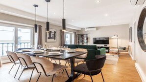 A modern living room with a dining area, large windows, a flat-screen TV, and a round mirror on the wall. - Nestled along the Que banks of Seine -perfection in intimate luxury near Louvre (Paris)