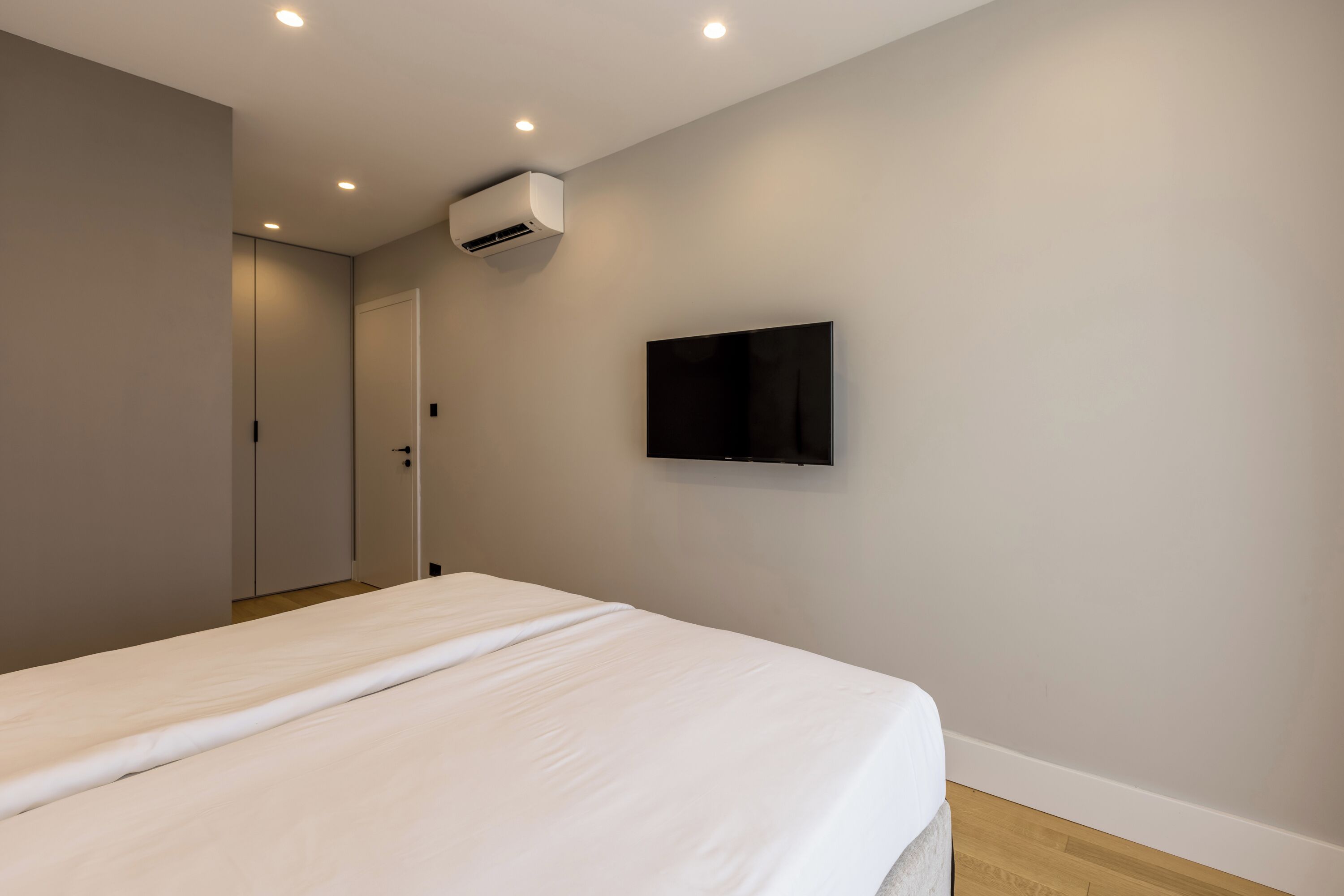 A bedroom with a bed, a mounted TV, and an air conditioning unit.