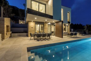 Una casa moderna de dos pisos con piscina, mobiliario exterior y un balcón.
