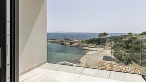 Varanda com vista clara para o mar, costa rochosa e um carro estacionado.