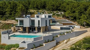 Uma villa moderna com piscina, vários níveis e vista para a floresta ao redor.