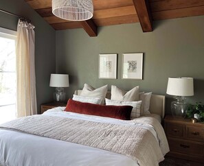 A bedroom with a bed, two bedside tables, a chandelier, and artwork on the wall.