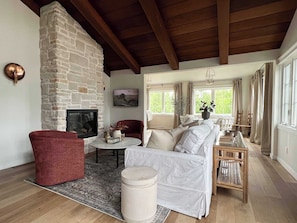 A living room with a stone fireplace, a red armchair, a white sofa, and a wooden coffee table. - Koselig Cottage: Charming 1950s Danish Cottage on 5 Acres (Ellison Bay)