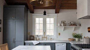 A kitchen with a white countertop, a sink with gold fixtures, and a stove. - Koselig Cottage: Charming 1950s Danish Cottage on 5 Acres (Ellison Bay)
