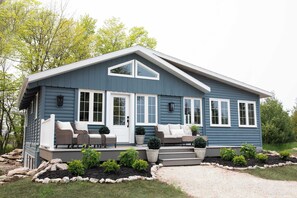 A blue house with a porch, white doors, and windows. There are steps leading to the porch, and potted plants are placed around the house.
