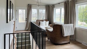 A room with a staircase, wicker furniture, a bed, and large windows. - Koselig Cottage: Charming 1950s Danish Cottage on 5 Acres (Ellison Bay)