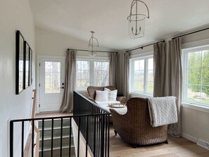 A room with a staircase, wicker furniture, a bed, and large windows.