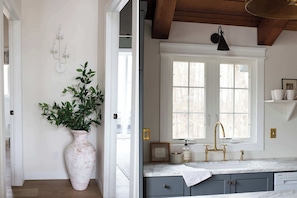 A kitchen with a window, a sink, and a vase with green leaves. - Koselig Cottage: Charming 1950s Danish Cottage on 5 Acres (Ellison Bay)