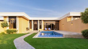 Ein modernes Haus mit Swimmingpool, einem gepflegten Rasen und einer Terrasse mit Gartenmöbeln.