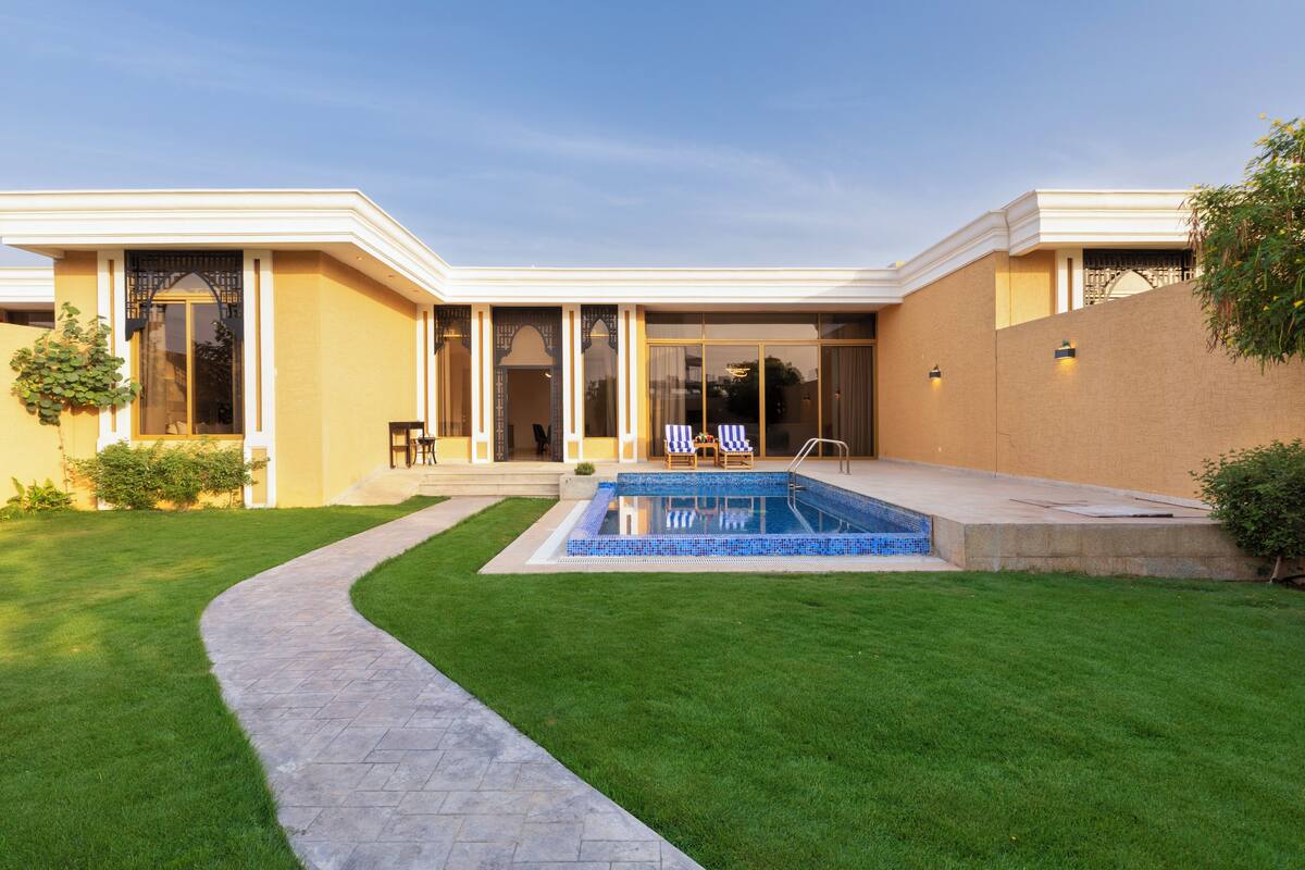 Une maison moderne dotée d’une piscine, d’une pelouse bien entretenue et d’un patio aménagé avec du mobilier d’extérieur.