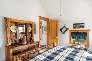 A rustic bedroom with a wooden dresser, a bed with plaid bedding, and a window with a view.