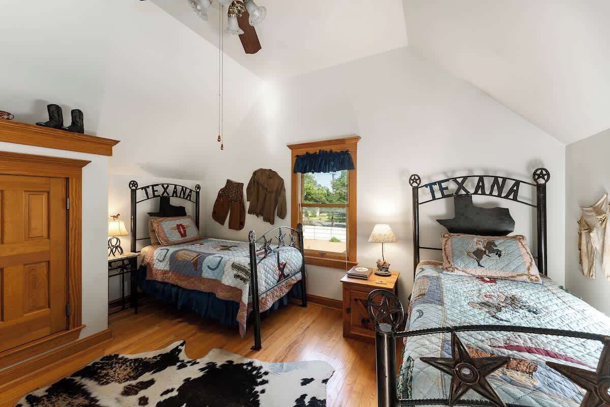 Ein Schlafzimmer mit zwei Betten, Holzböden, einem Kuhfellteppich und einem Fenster mit Blick ins Grüne.