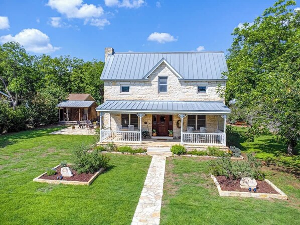A two-story stone house with a metal roof, a front porch, and a stone pathway leading to the entrance.