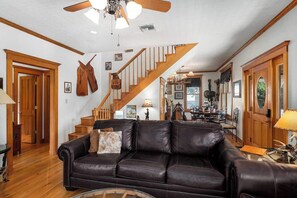 A spacious living room with a leather sofa, wooden staircase, and a dining area.