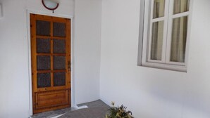 Une pièce avec une porte en bois, une fenêtre avec des rideaux et une plante en pot posée sur le sol.